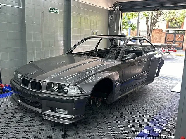 Carrocería del BMW M3 E36 desarmada, sin ruedas ni puertas, en el taller de ADM TEAM