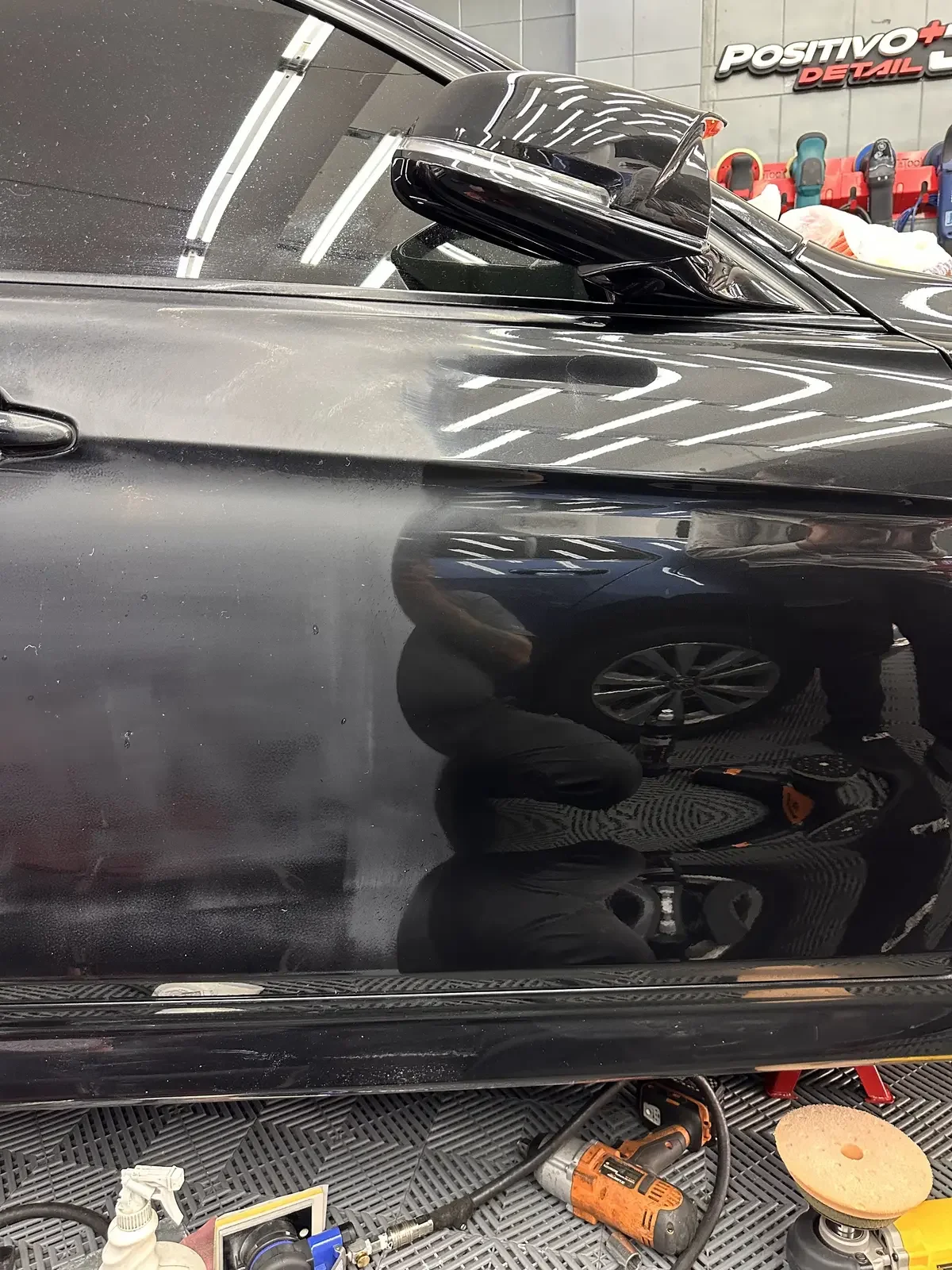 Lateral de un auto negro durante la corrección de pintura en ADM TEAM, con las pulidoras y los pads en el piso