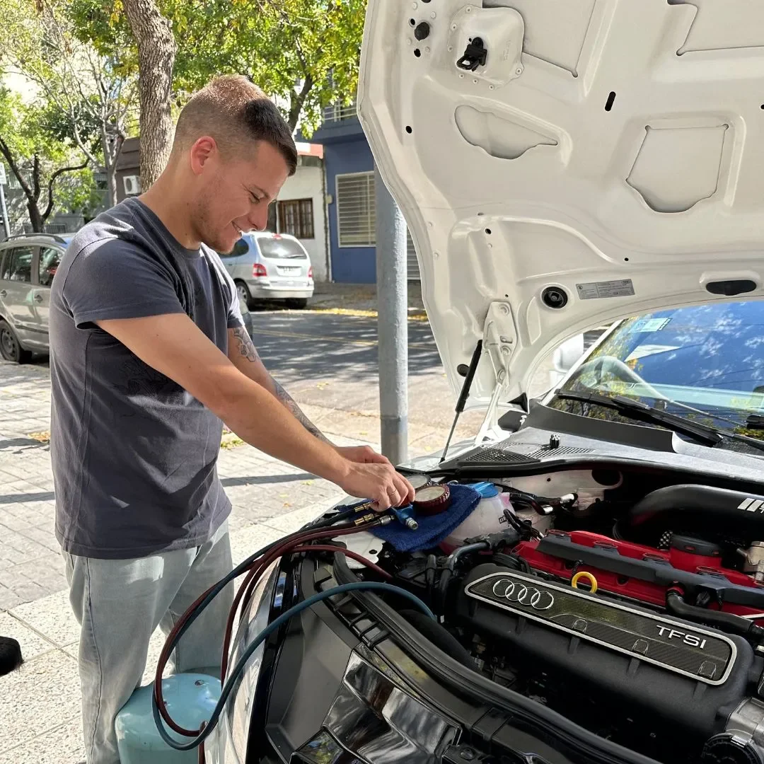 Técnico de ADM TEAM revisando el vano motor de un auto con el capot abierto, en la vereda del taller