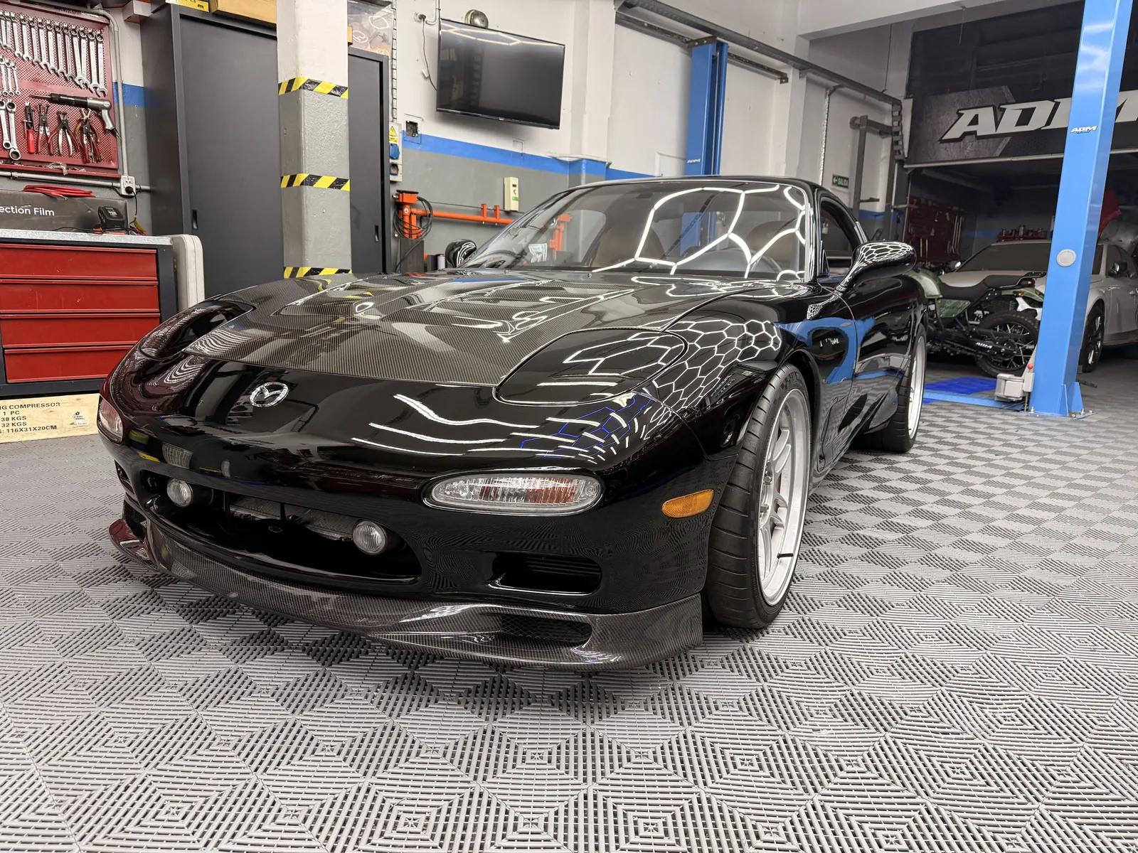 Mazda RX-7 FD negro en el taller de ADM TEAM, vista tres cuartos delantera